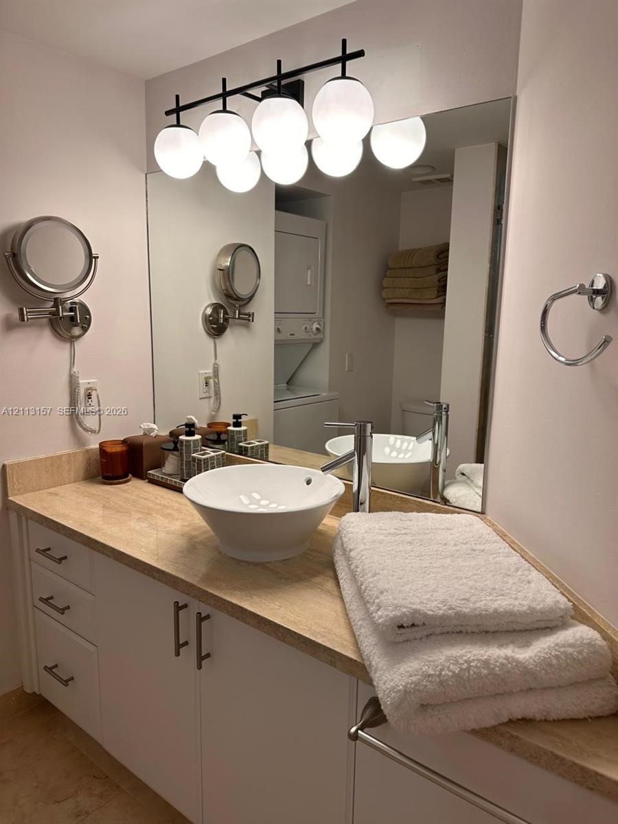 Bathroom vanity featuring a light-toned stone countertop, white cabinetry with metallic hardware, a vessel sink with a single-handle chrome faucet, an