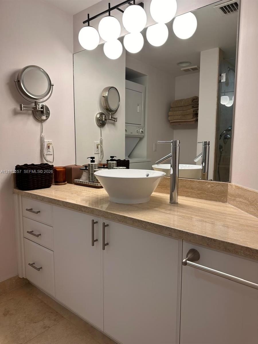 White vanity cabinetry with metal pulls, stone countertop, vessel sink with a high-arch faucet, wall-to-wall mirror, and multi-globe light fixture