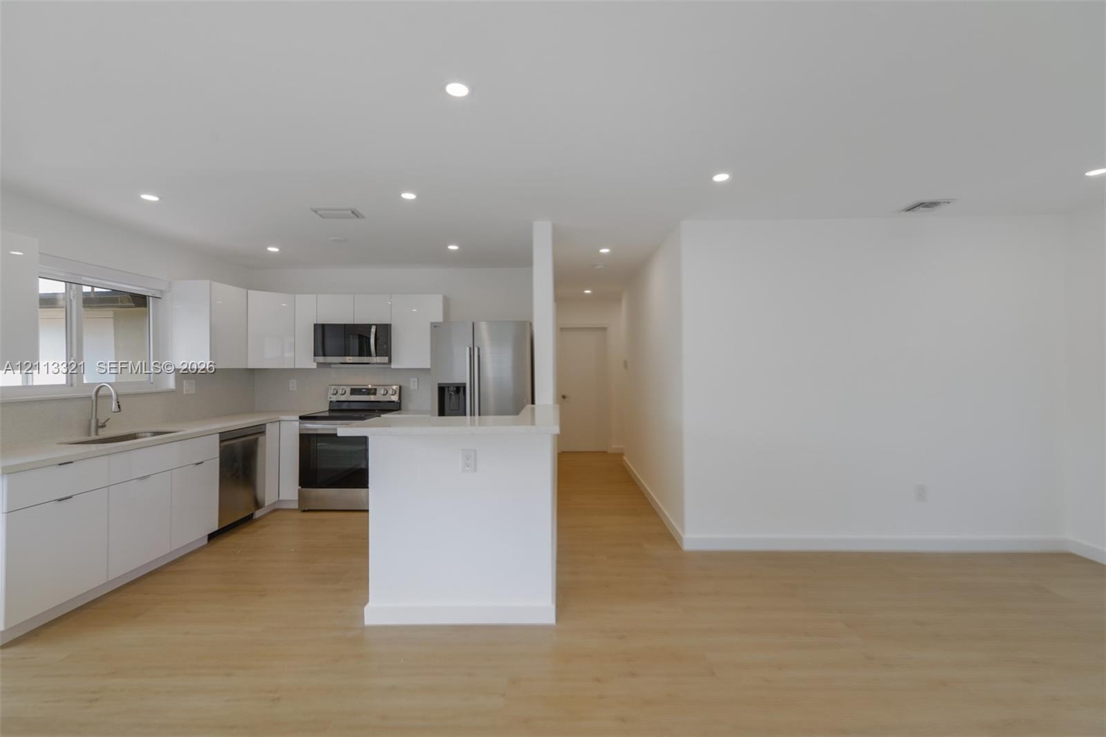 Kitchen featuring white high-gloss cabinetry, stainless steel appliances, a peninsula with stone countertops, and wood-finish flooring illuminated by 