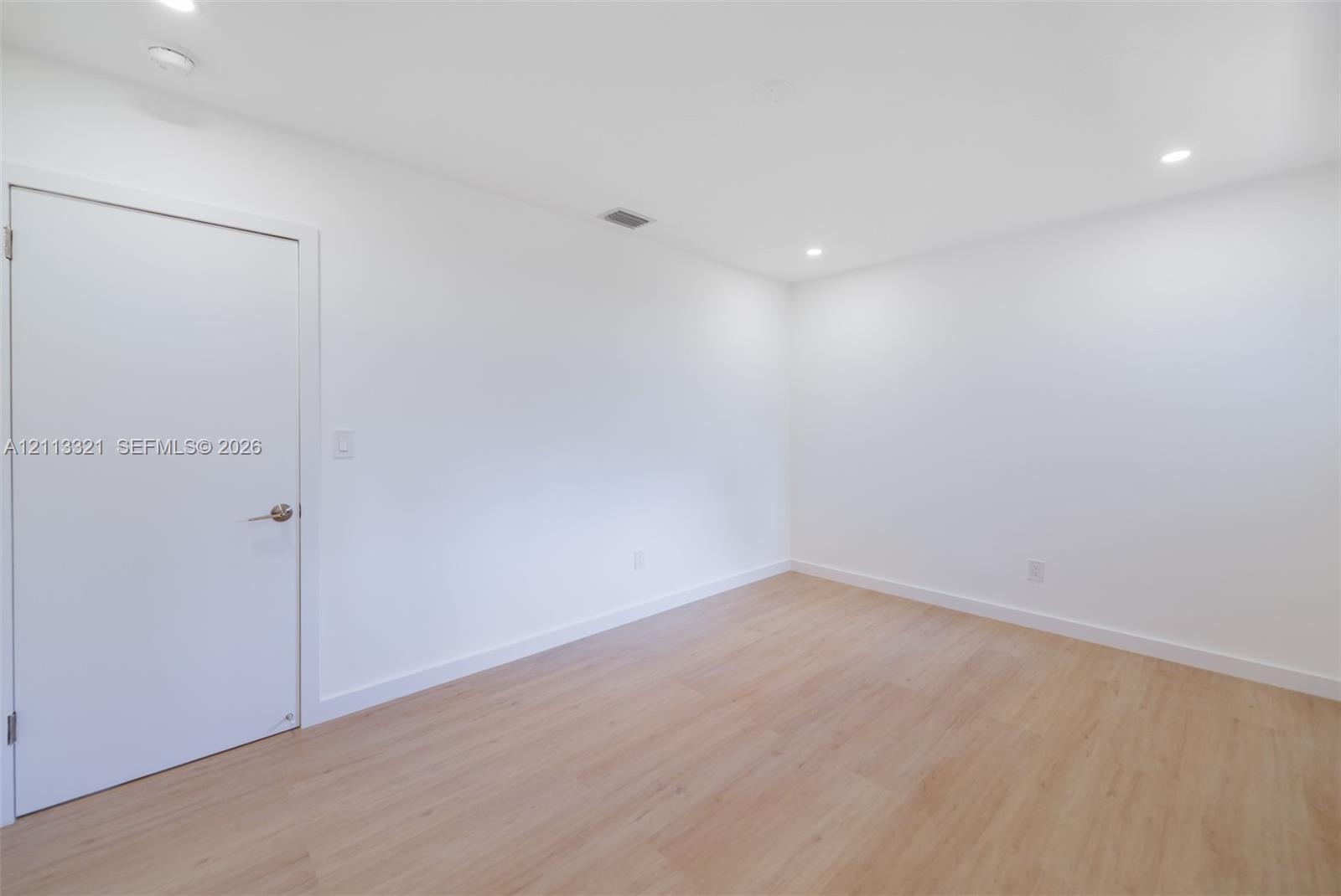 Neutral interior space featuring wood-finish flooring, crisp white walls, and recessed ceiling lighting