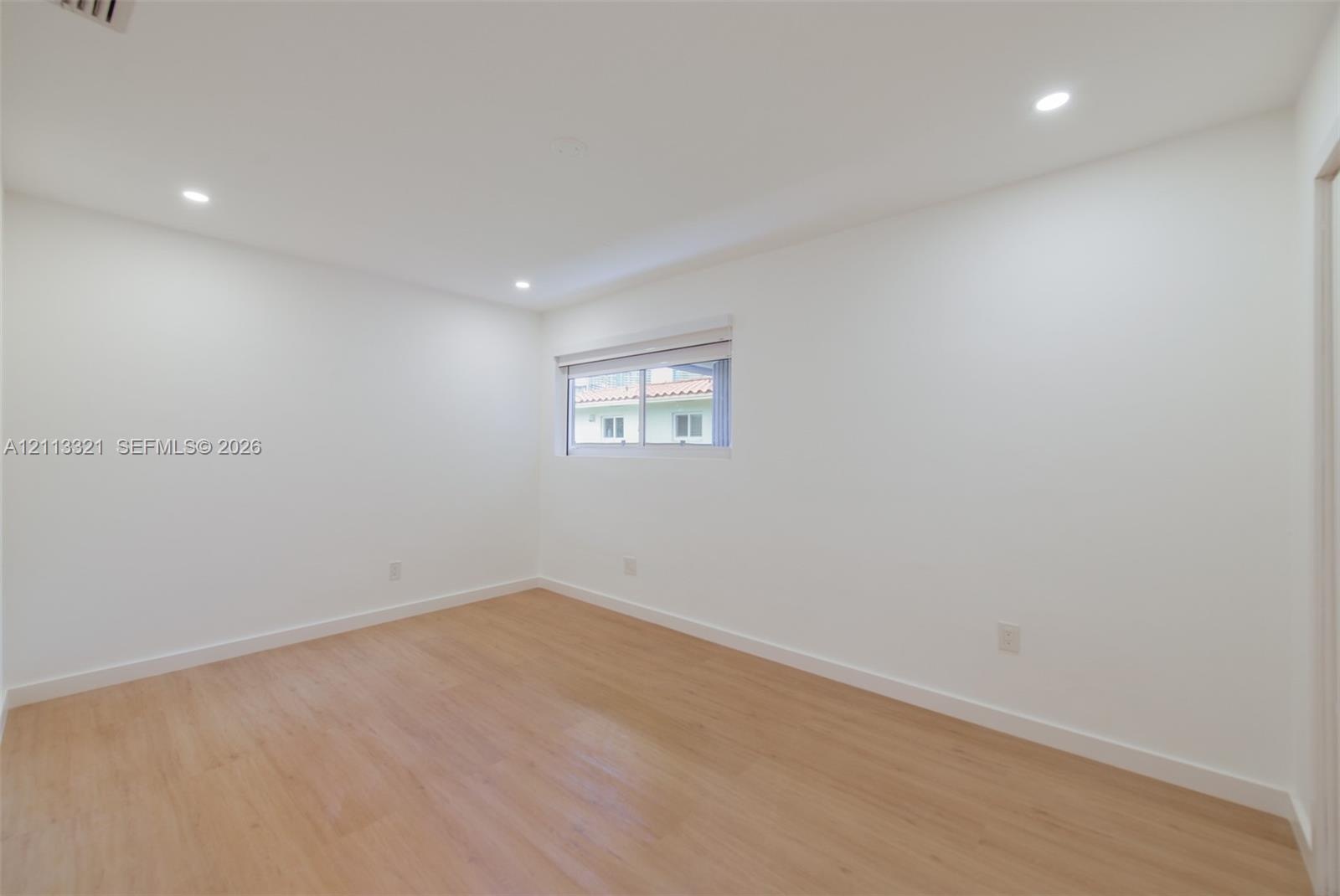 Neutral interior room featuring wood-finish flooring, recessed lighting, and a window with a horizontal blind