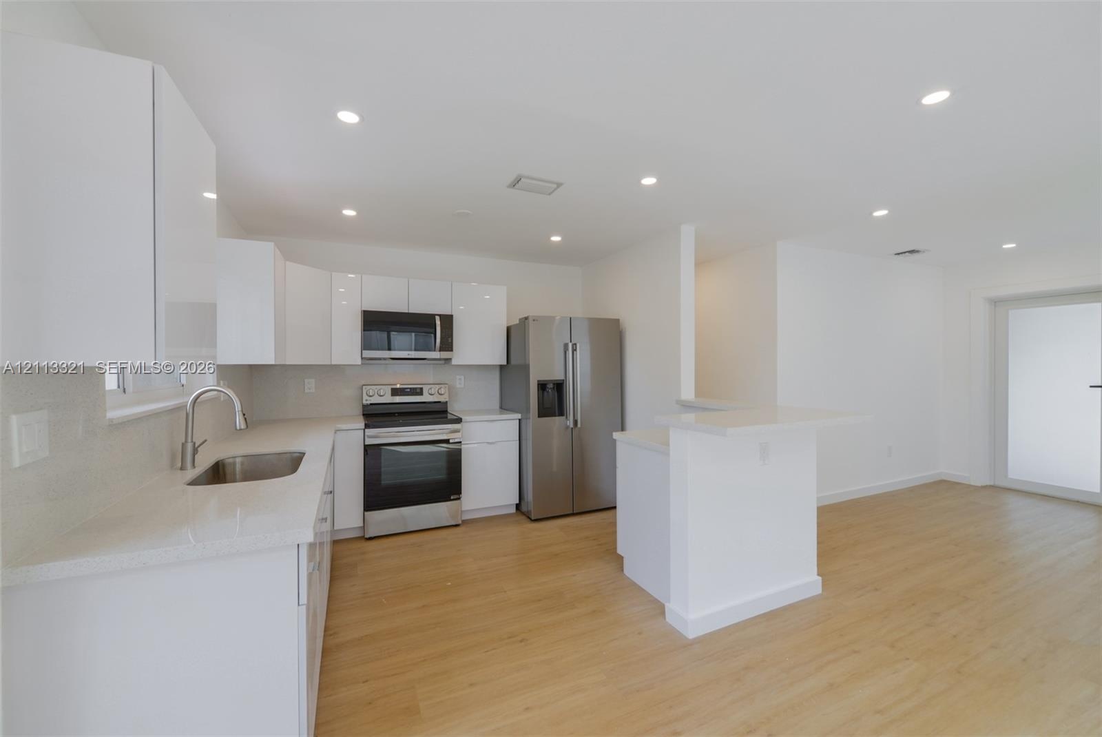 Kitchen featuring high-gloss white cabinetry, stone-finish countertops, stainless steel appliances, recessed lighting, and wood-finish flooring