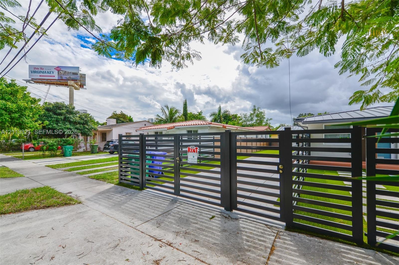 Black metal horizontal-slat gate with a concrete driveway and mature trees