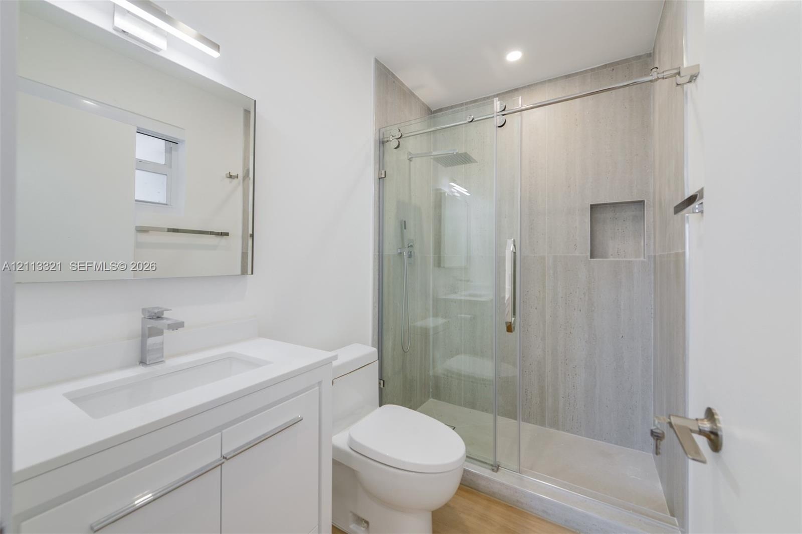 Bathroom featuring a white vanity with a countertop basin, a frameless glass shower enclosure with sliding doors, a recessed wall niche, and large-for