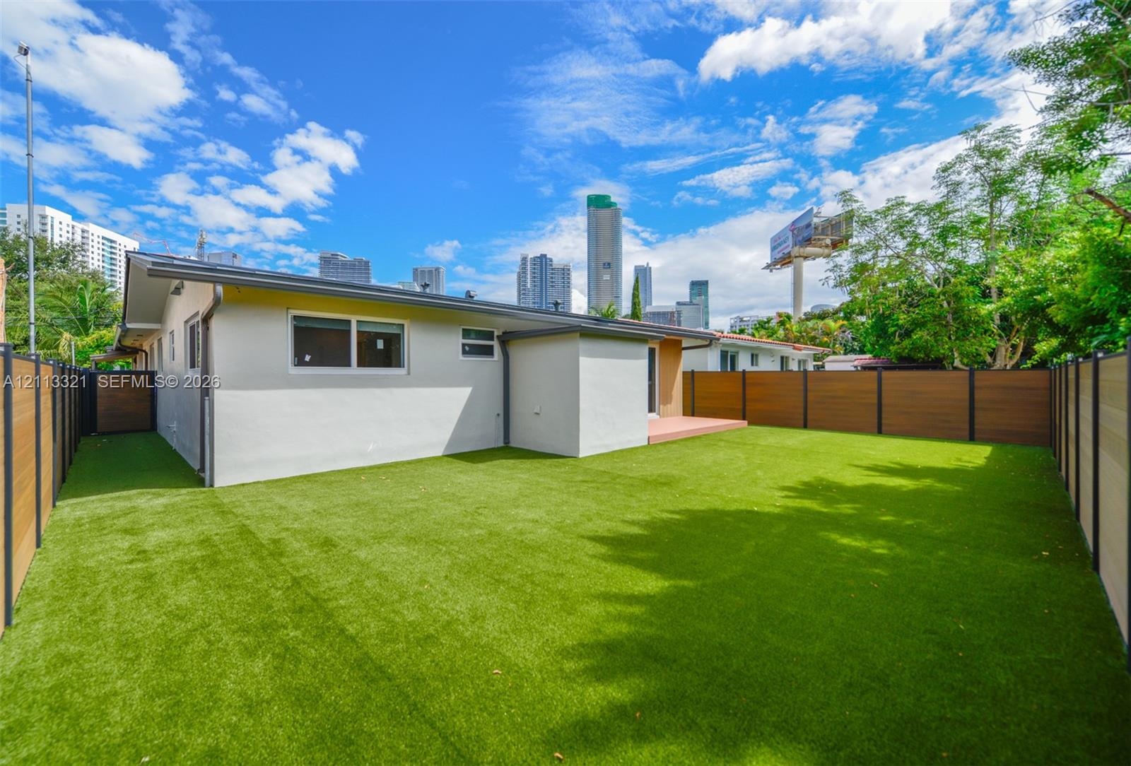 Rear exterior featuring synthetic turf lawn, horizontal wood-finish privacy fencing, and a concrete patio