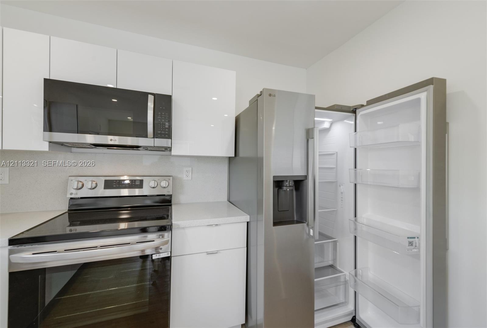 Kitchen featuring high-gloss white flat-panel cabinetry, stone-finish countertops, stainless steel microwave, stainless steel slide-in range, and stai