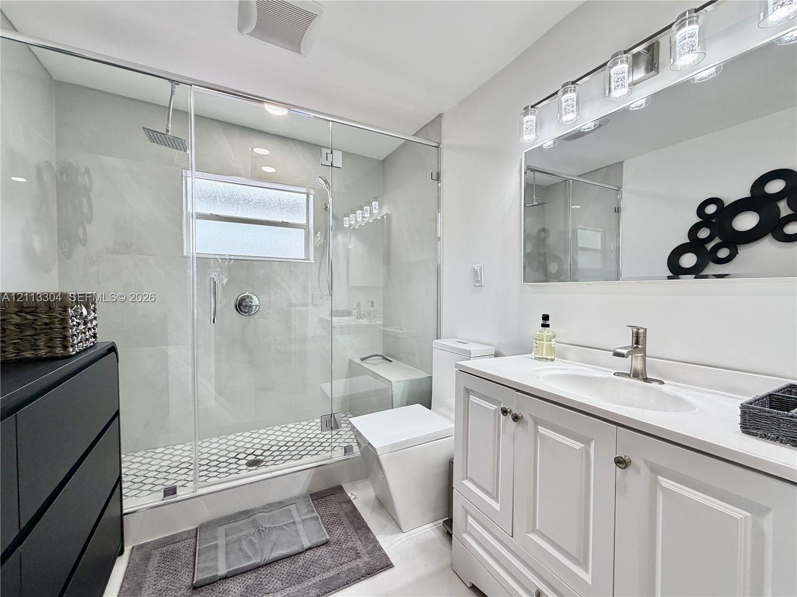 Bathroom featuring a frameless glass-enclosed shower with large-format wall tile and hexagonal floor tile, a white vanity cabinet with an integrated s