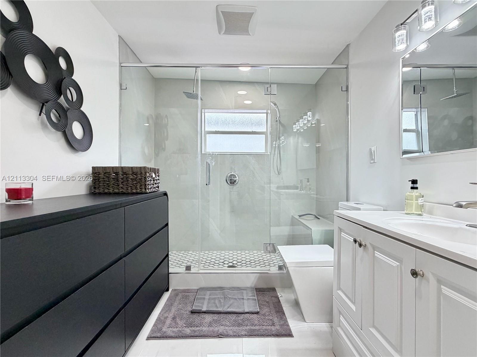 Walk-in shower with a glass enclosure, rainfall showerhead, and hexagonal tile flooring, paired with a white vanity featuring an integrated sink and c