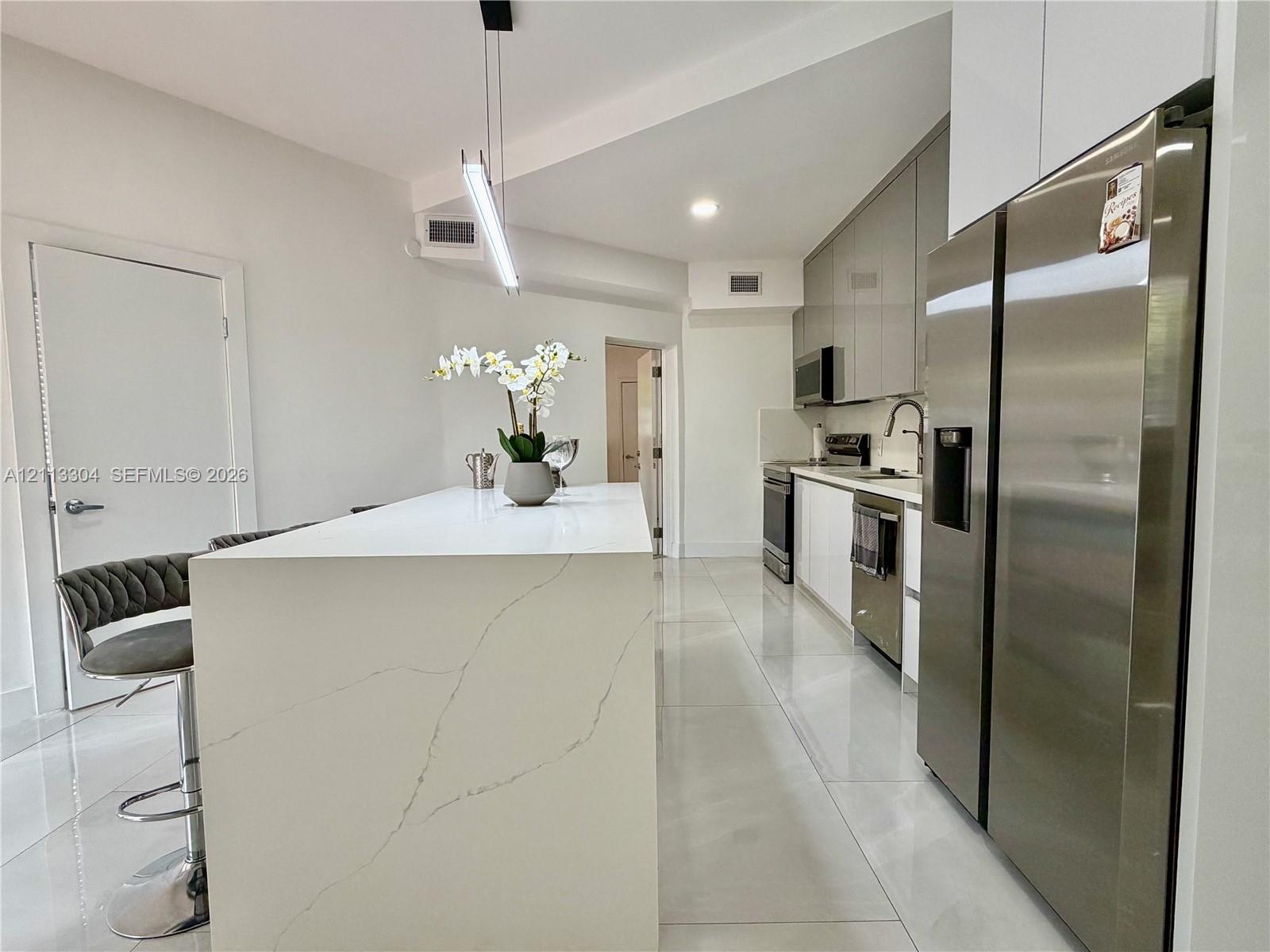 Kitchen featuring a waterfall-edge island with stone-finish countertop, high-gloss flat-panel cabinetry, stainless steel appliances, and large-format 