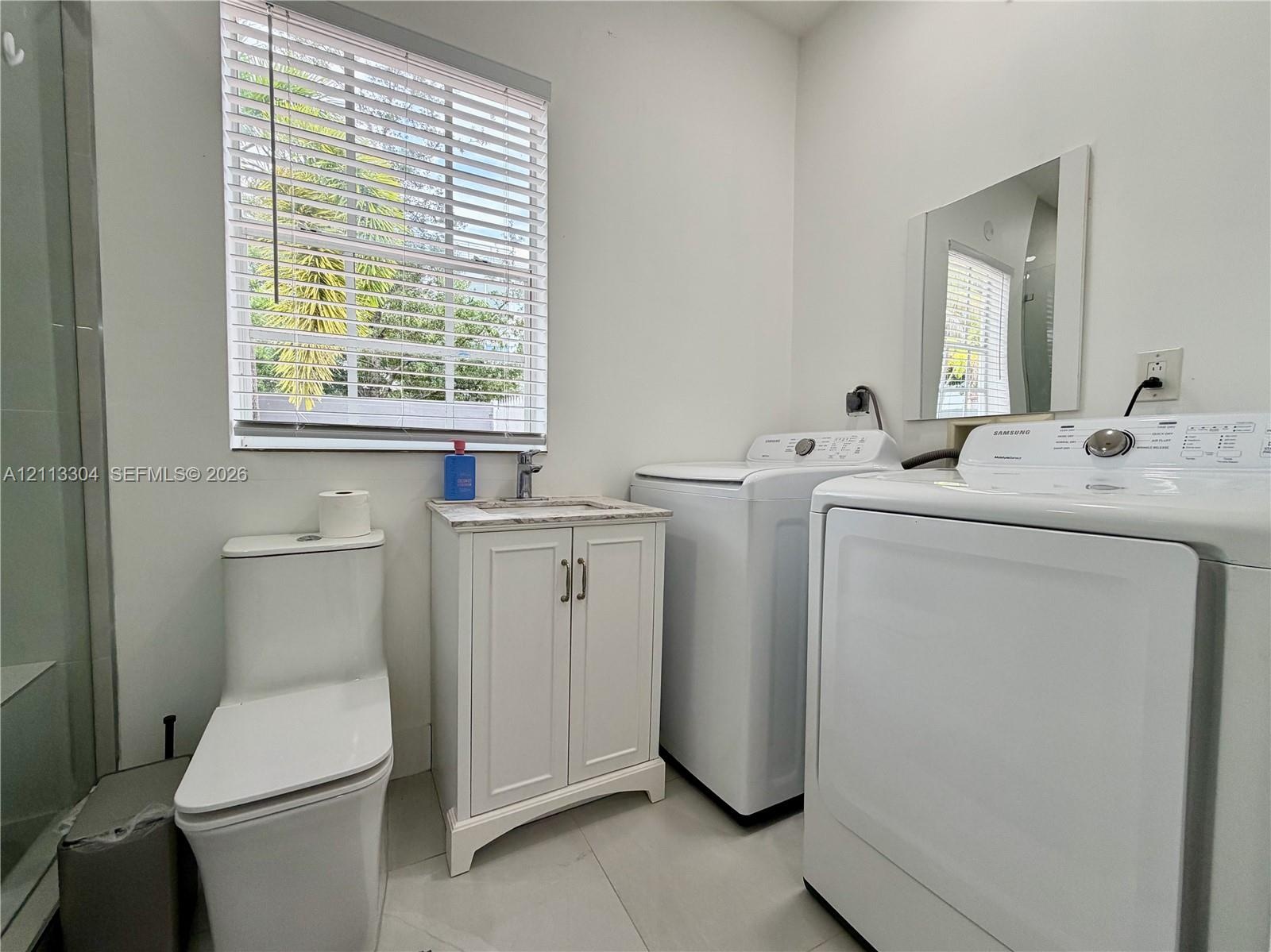 Bathroom featuring a floor-mounted toilet, vanity with a stone-finish countertop and integrated sink, wall-mounted mirror, and tile flooring