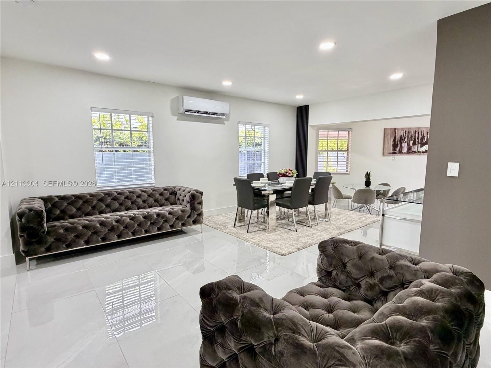 Large-format tile flooring, recessed ceiling lighting, wall-mounted ductless air conditioning unit, and multiple windows with white blinds