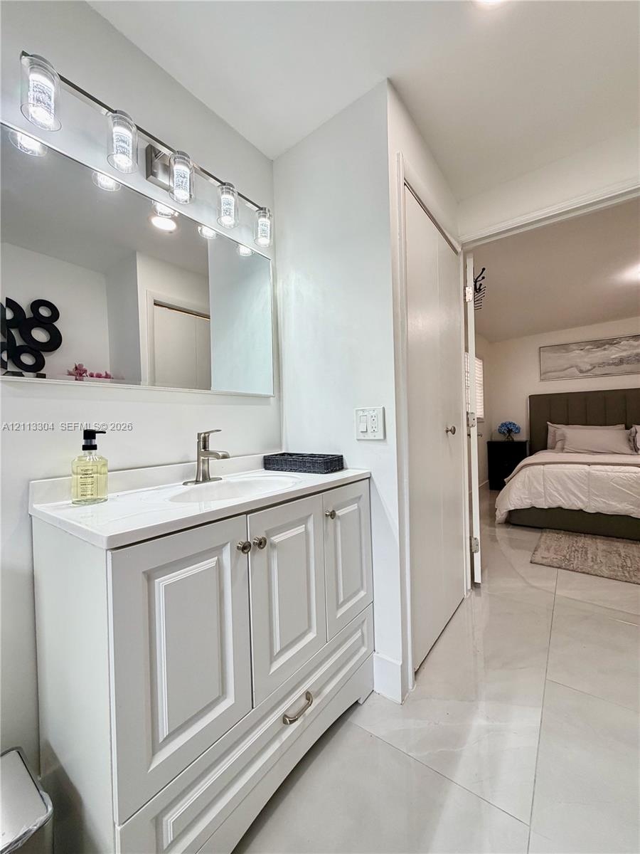 White vanity with shaker-style cabinetry, solid-surface countertop with an integrated sink, polished metal hardware, and a multi-bulb light fixture mo