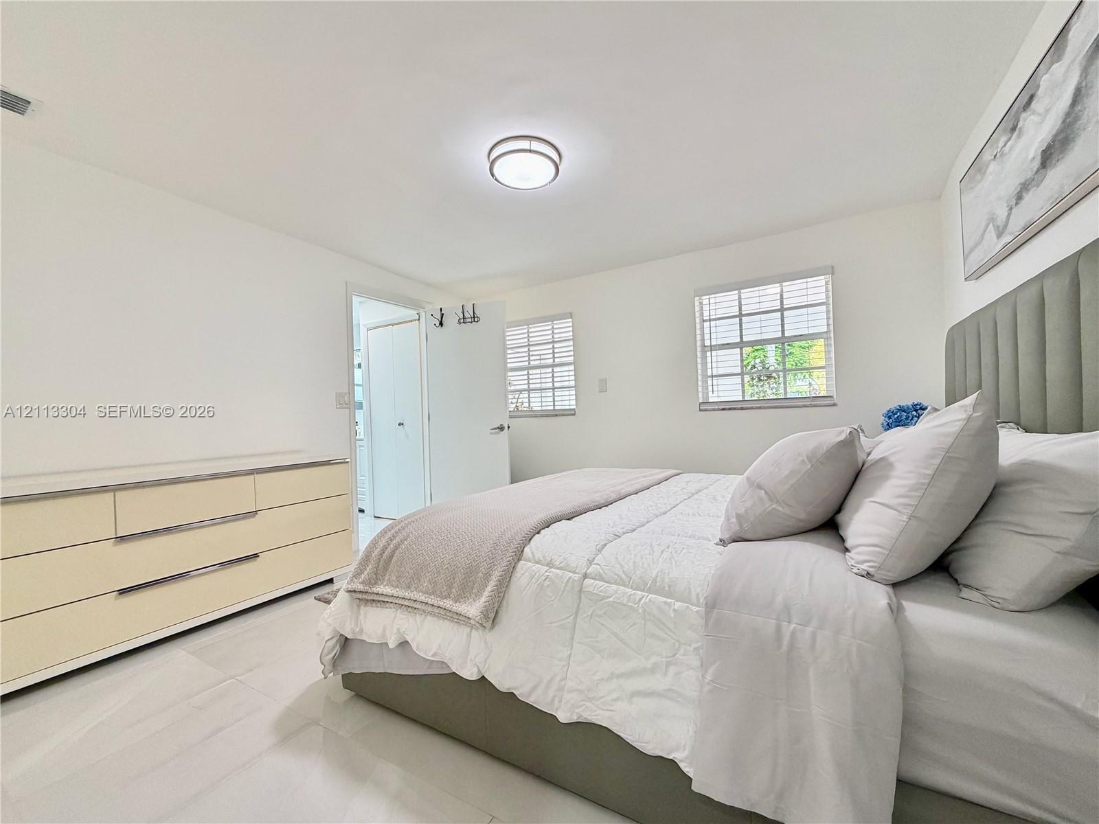 Neutral-toned interior featuring large-format tile flooring, dual-pane windows with horizontal blinds, and a circular flush-mount ceiling light fixtur