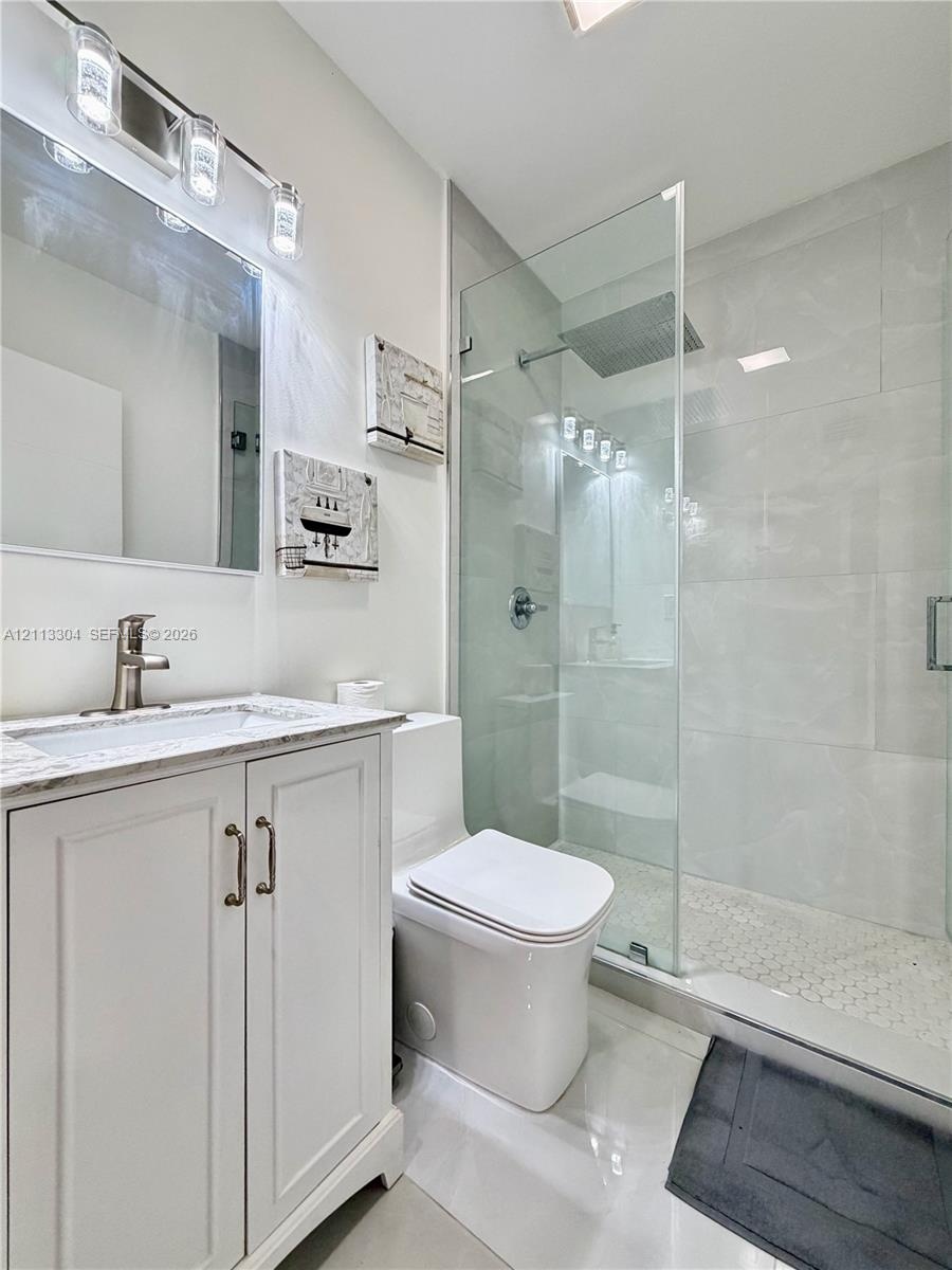 Bathroom featuring a white shaker-style vanity with a stone countertop, an integrated sink with a metallic faucet, a frameless glass-enclosed walk-in 
