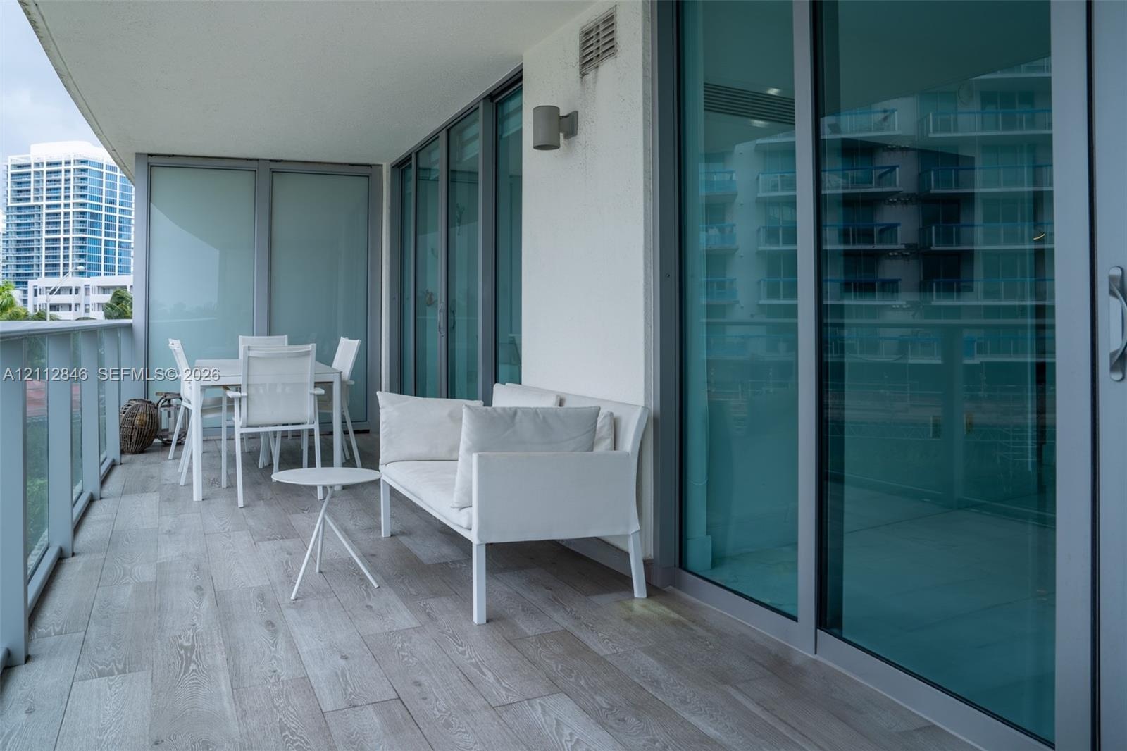 Covered balcony featuring wood-finish flooring, glass-panel railings, and floor-to-ceiling sliding glass doors