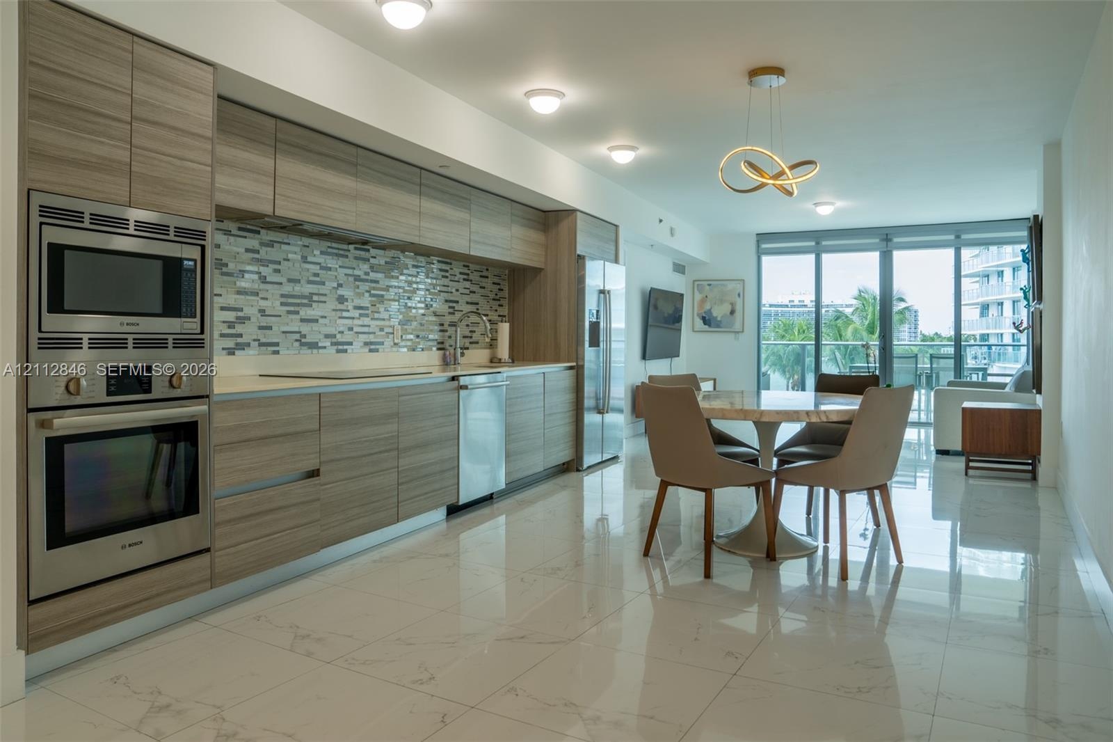 Contemporary kitchen featuring wood-finish cabinetry, stainless steel built-in oven and microwave, mosaic tile backsplash, and polished stone-finish f