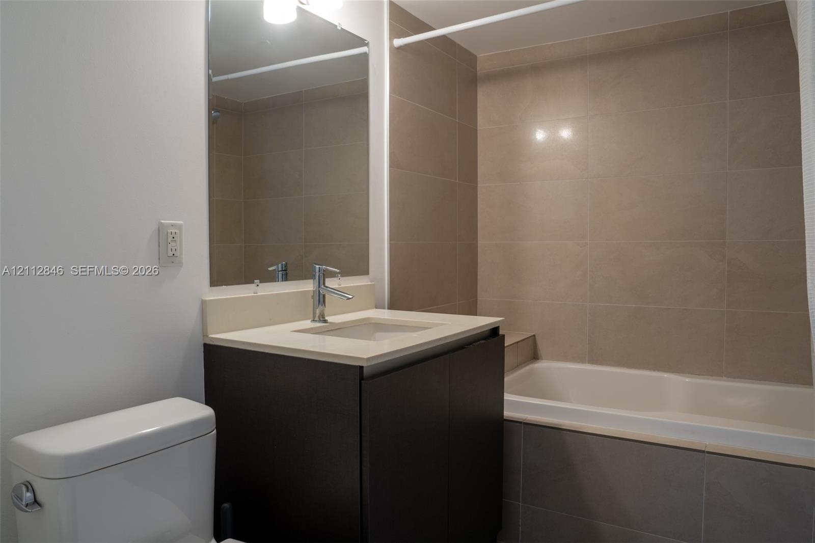 Bathroom featuring a dark wood-finish vanity, integrated sink with light-toned solid surface countertop, rectangular wall mirror, and a bathtub enclos