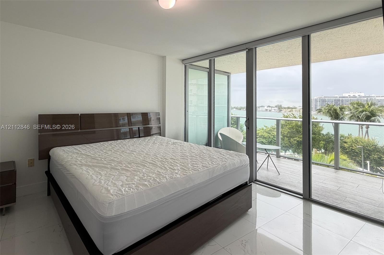 Floor-to-ceiling sliding glass doors, white tile flooring, and private balcony with metal railing and water scenery