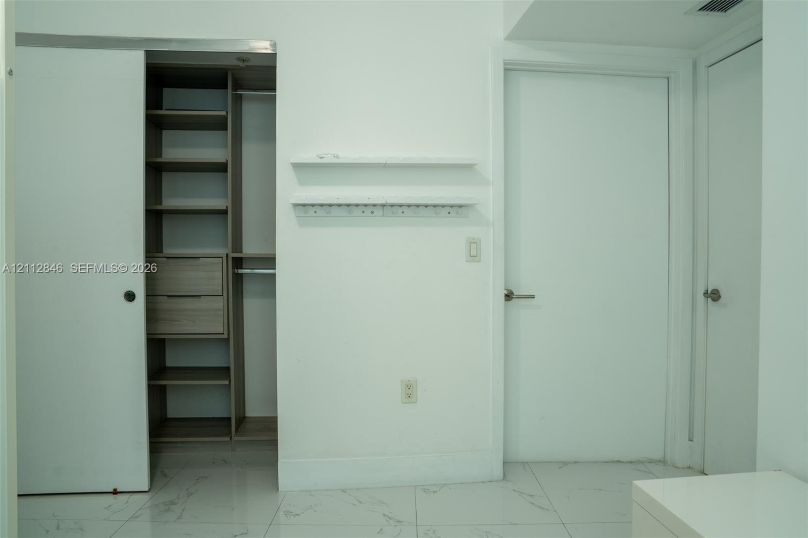 Walk-in closet featuring custom wood-finish shelving and built-in drawers, set against polished white tile flooring