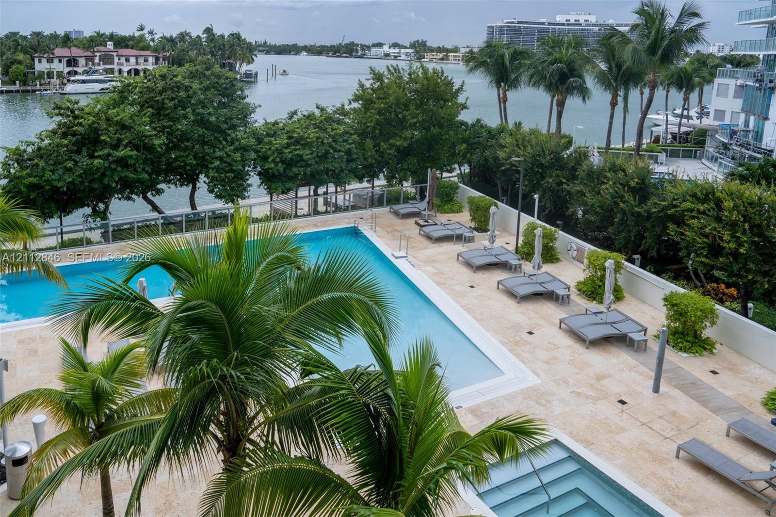 Waterfront pool and spa area featuring natural stone decking, integrated palm tree landscaping, and perimeter glass railing