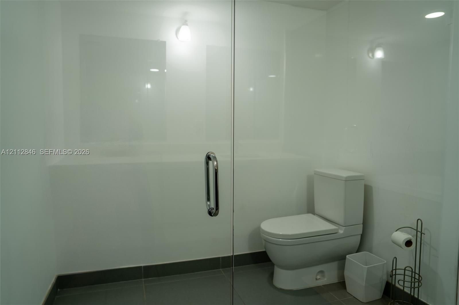 Glass-enclosed shower with white panel wall surrounds, chrome handle hardware, and large-format tile flooring