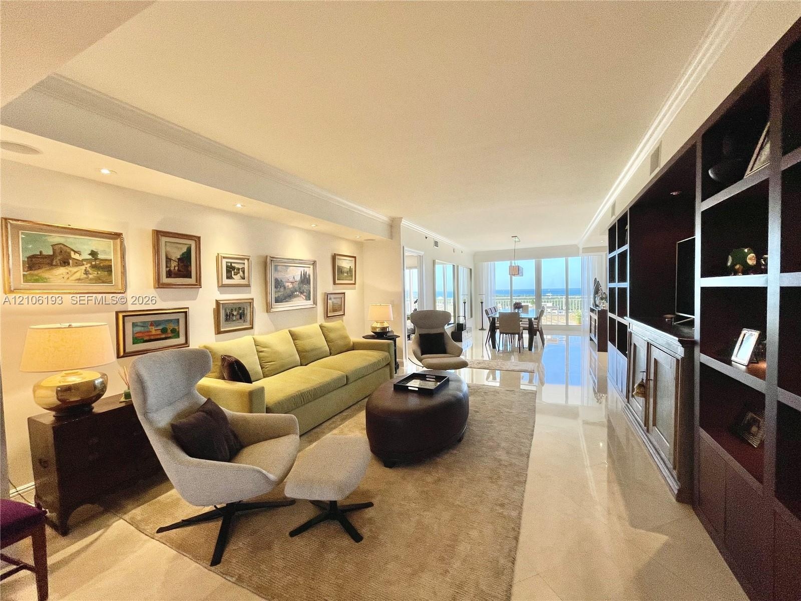 Open-concept living space featuring large-format polished stone flooring, custom floor-to-ceiling dark wood built-in cabinetry, recessed perimeter lig