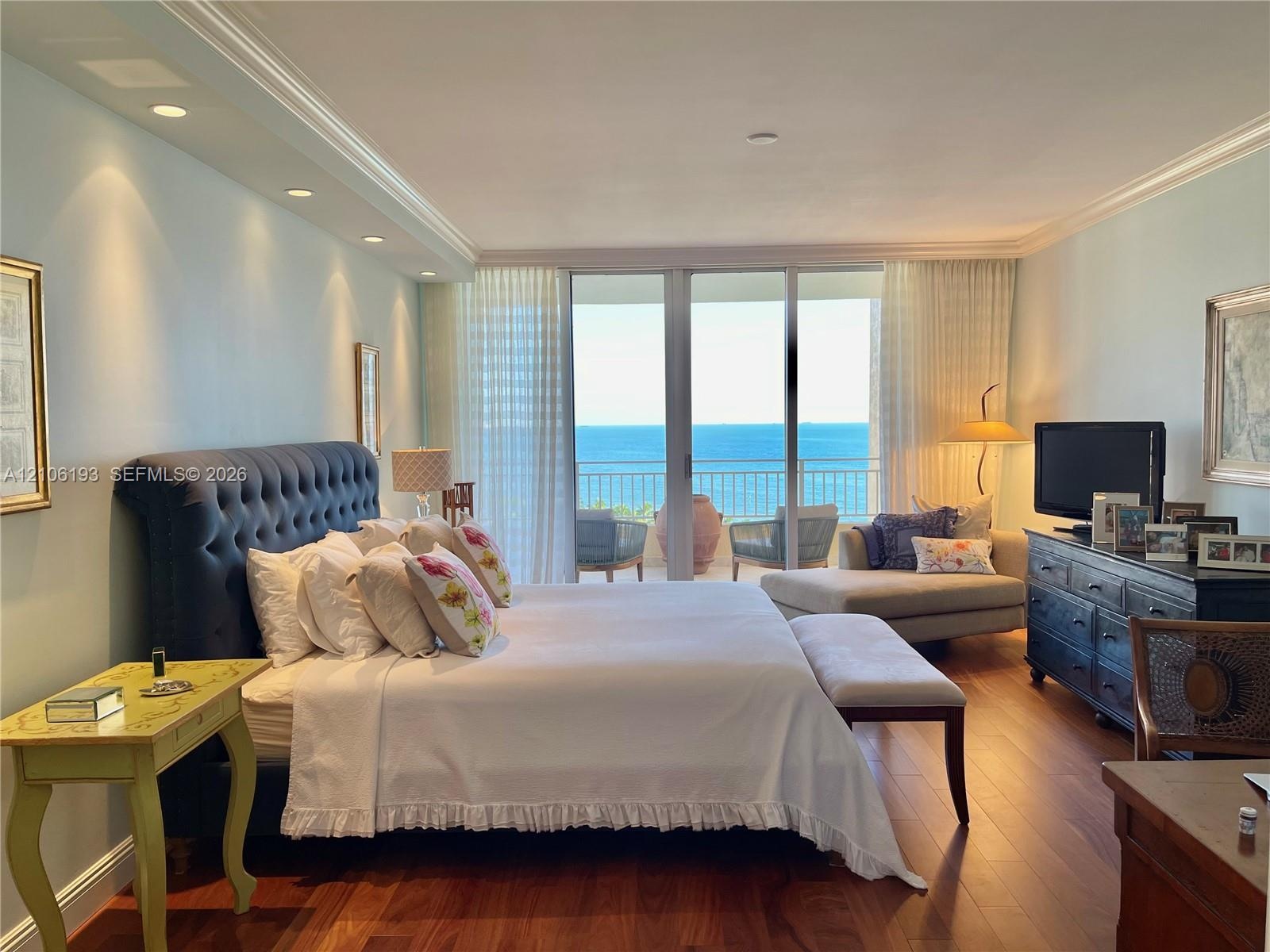 Bedroom featuring wood-finish flooring, recessed lighting, crown molding, and floor-to-ceiling glass sliding doors opening to a balcony with ocean exp