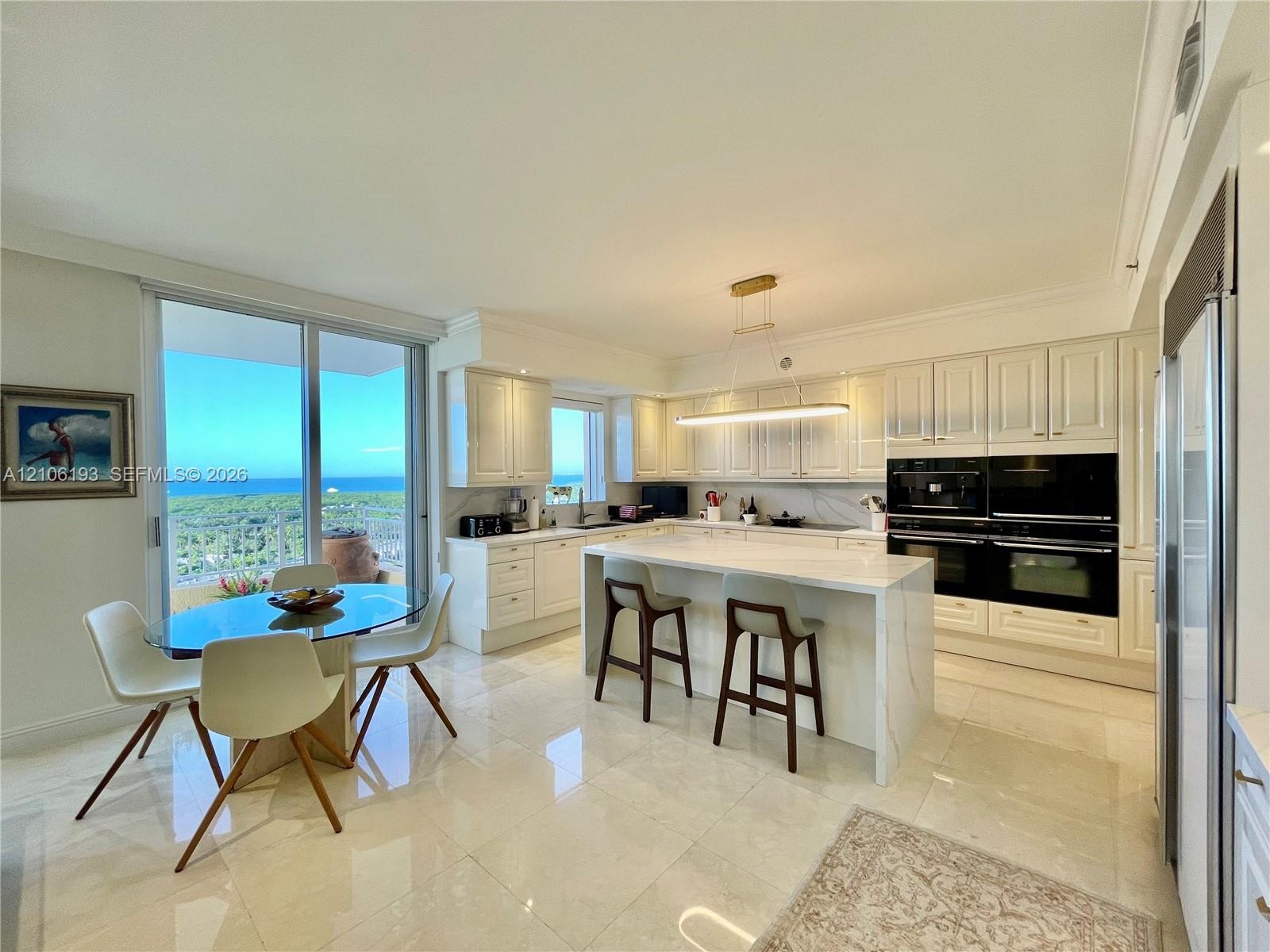 Kitchen featuring white cabinetry, an expansive center island with stone-finish countertops, built-in dual ovens, polished tile flooring, and sliding 