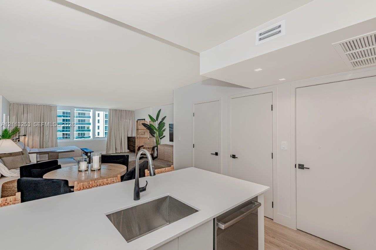 Kitchen island featuring a solid-surface countertop, stainless steel undermount sink, and matte black faucet, complemented by wood-finish flooring and