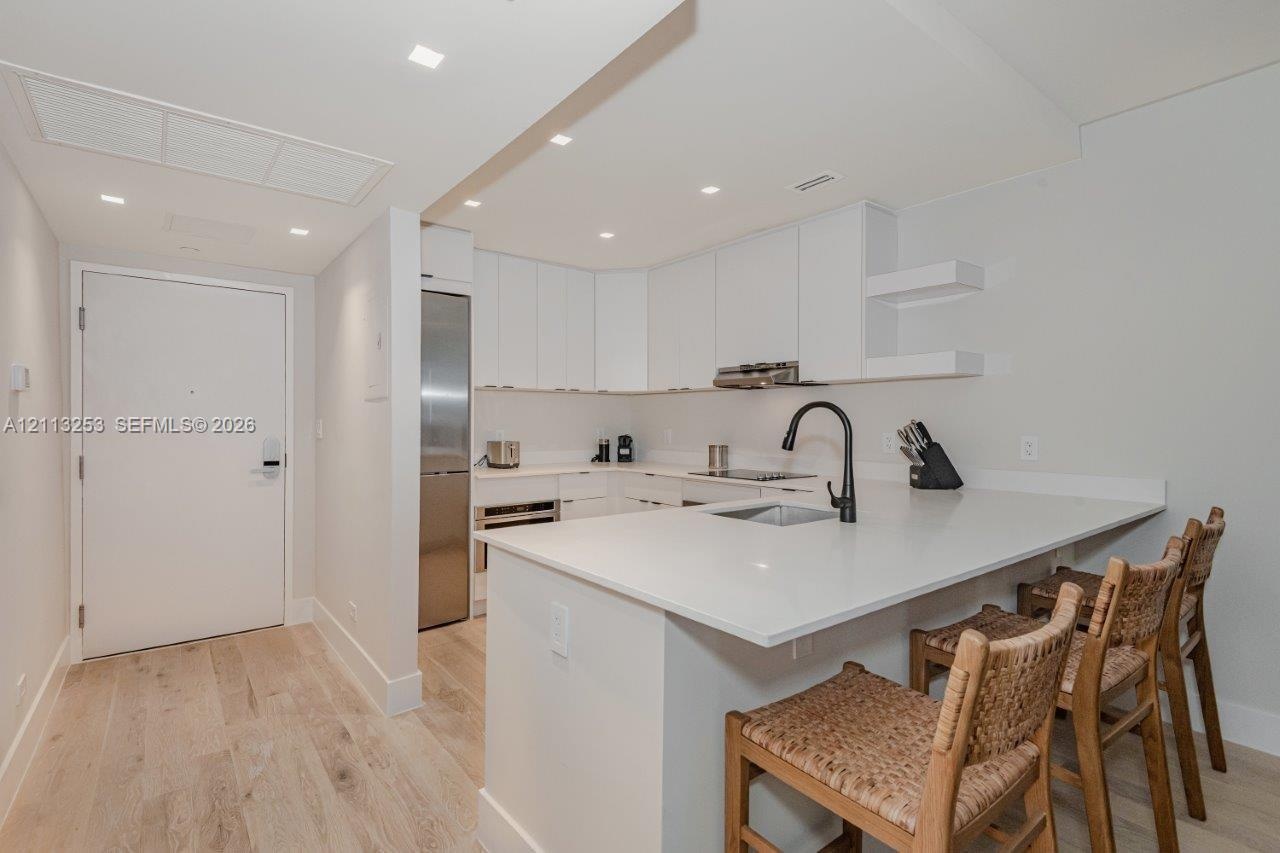 Kitchen featuring flat-panel cabinetry, light-toned countertops, a matte black high-arch faucet, integrated stainless steel appliances, and wood-finis