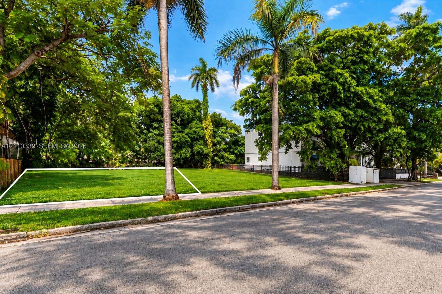 Cleared residential lot featuring manicured lawn, established palm trees, and mature shade trees
