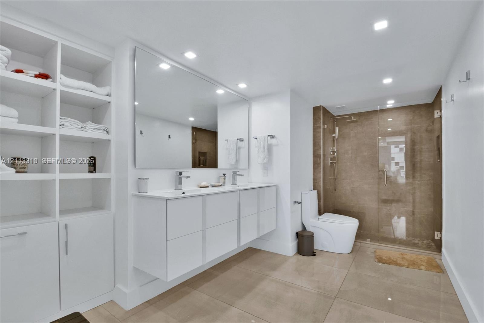 Bathroom featuring a floating double vanity with rectangular sinks, a floor-to-ceiling white built-in storage cabinet, large-format tile flooring, and