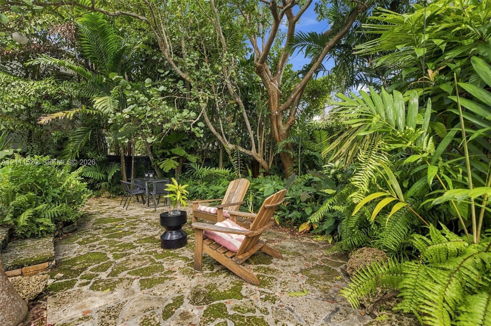 Flagstone patio featuring mature landscaping, dense tropical foliage, and large specimen trees