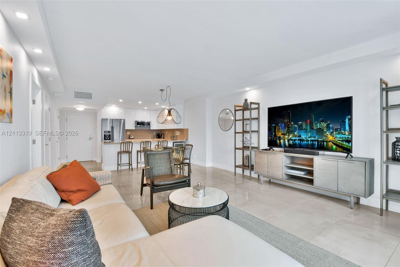 Open-concept living space featuring high-gloss white cabinetry, polished tile flooring, recessed ceiling lighting, and a breakfast bar