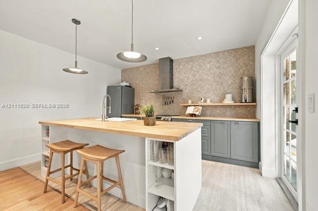 Kitchen featuring a wood-topped island with open shelving, herringbone-patterned tile backsplash, stainless steel range hood, grey shaker-style cabine
