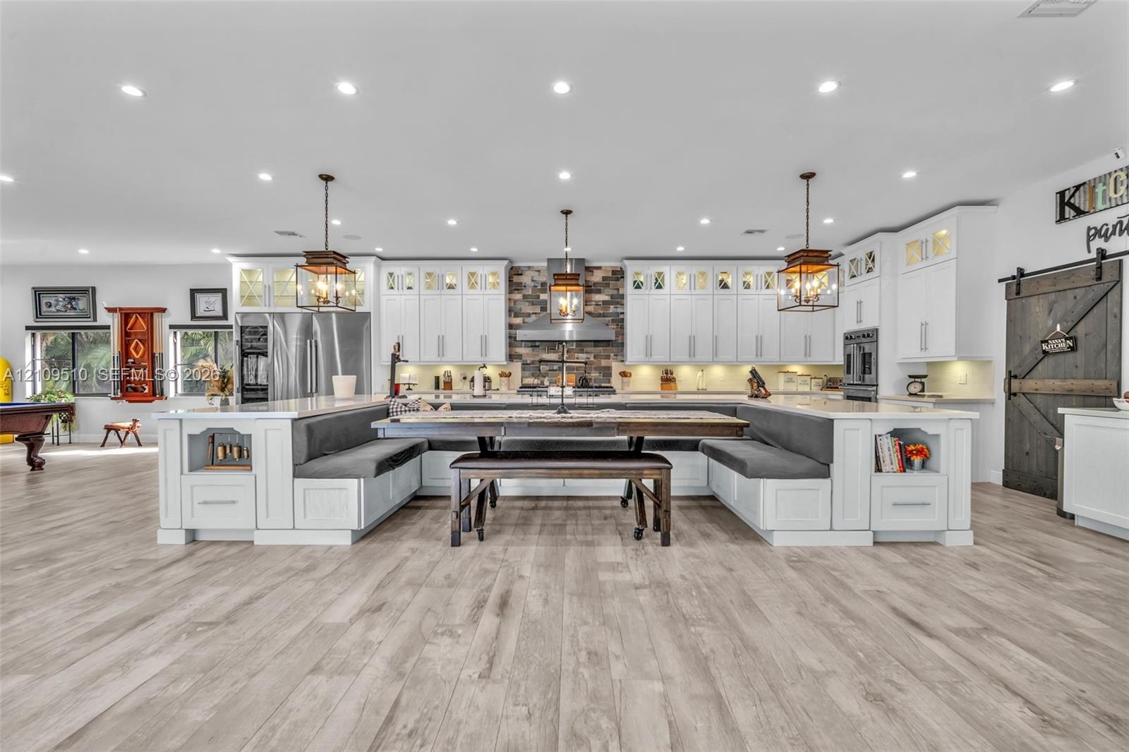 Kitchen featuring white cabinetry, wood-finish flooring, a stone-tiled backsplash, integrated banquet seating, and a sliding barn door