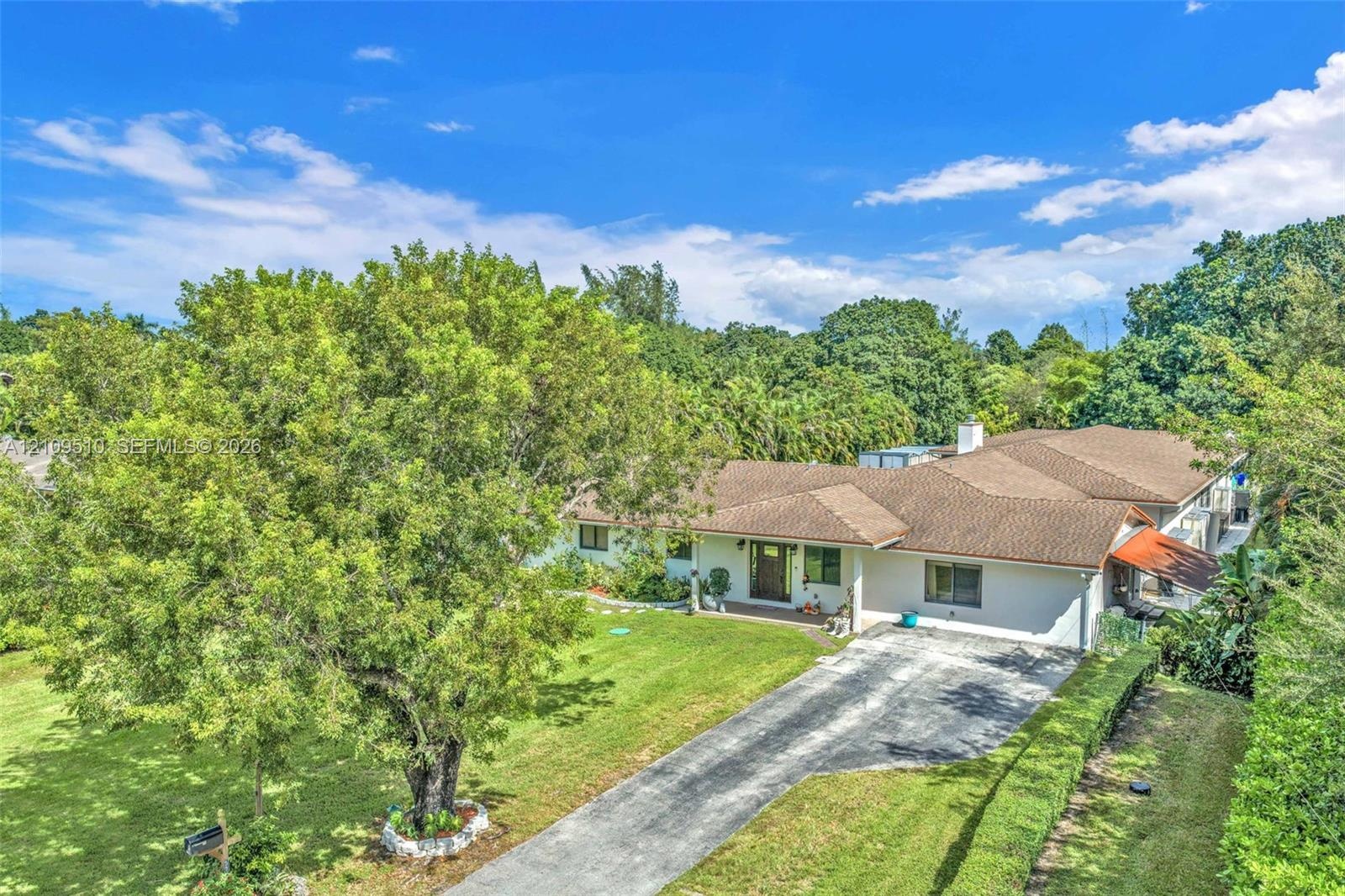 Single-story residence featuring a multi-gabled shingle roof, expansive front lawn, mature trees, and a paved driveway