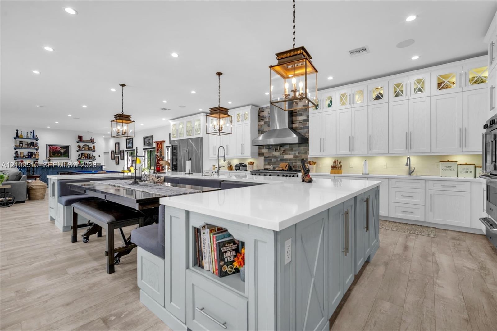 Kitchen featuring shaker-style cabinetry with glass-panel upper doors, a large central island with integrated storage, white quartz countertops, wood-
