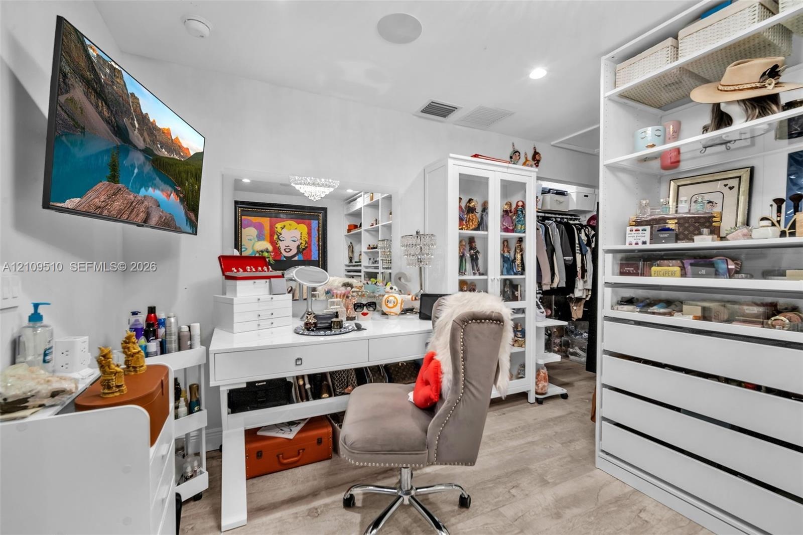 Walk-in closet featuring white custom built-in cabinetry, glass-front display shelving, integrated drawer units, and wood-finish flooring