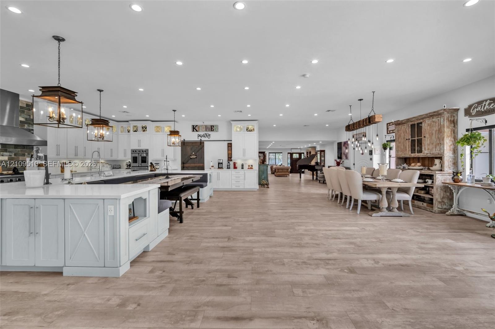 Open-concept space featuring wood-finish flooring, extensive recessed lighting, white shaker-style cabinetry, a large kitchen island with quartz count