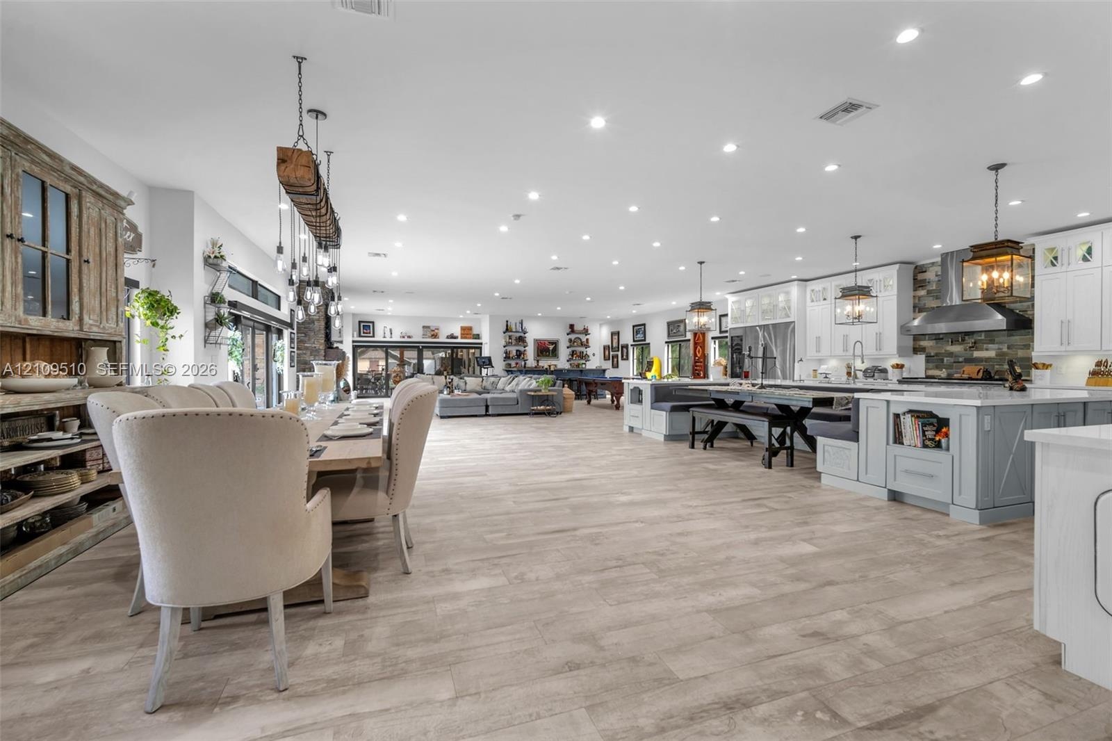 Open-concept layout featuring wood-finish flooring, a kitchen island with built-in booth seating, recessed lighting, and custom cabinetry