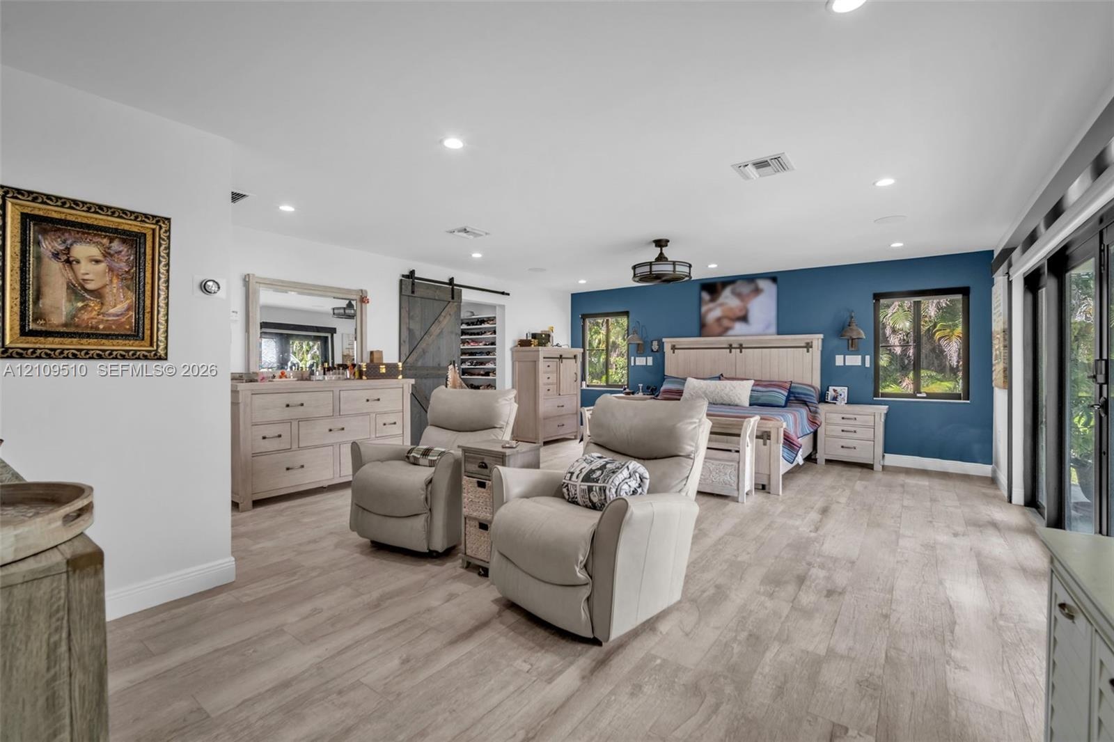 Wood-finish flooring, sliding barn door, recessed lighting, ceiling fan with integrated lighting, and multiple windows