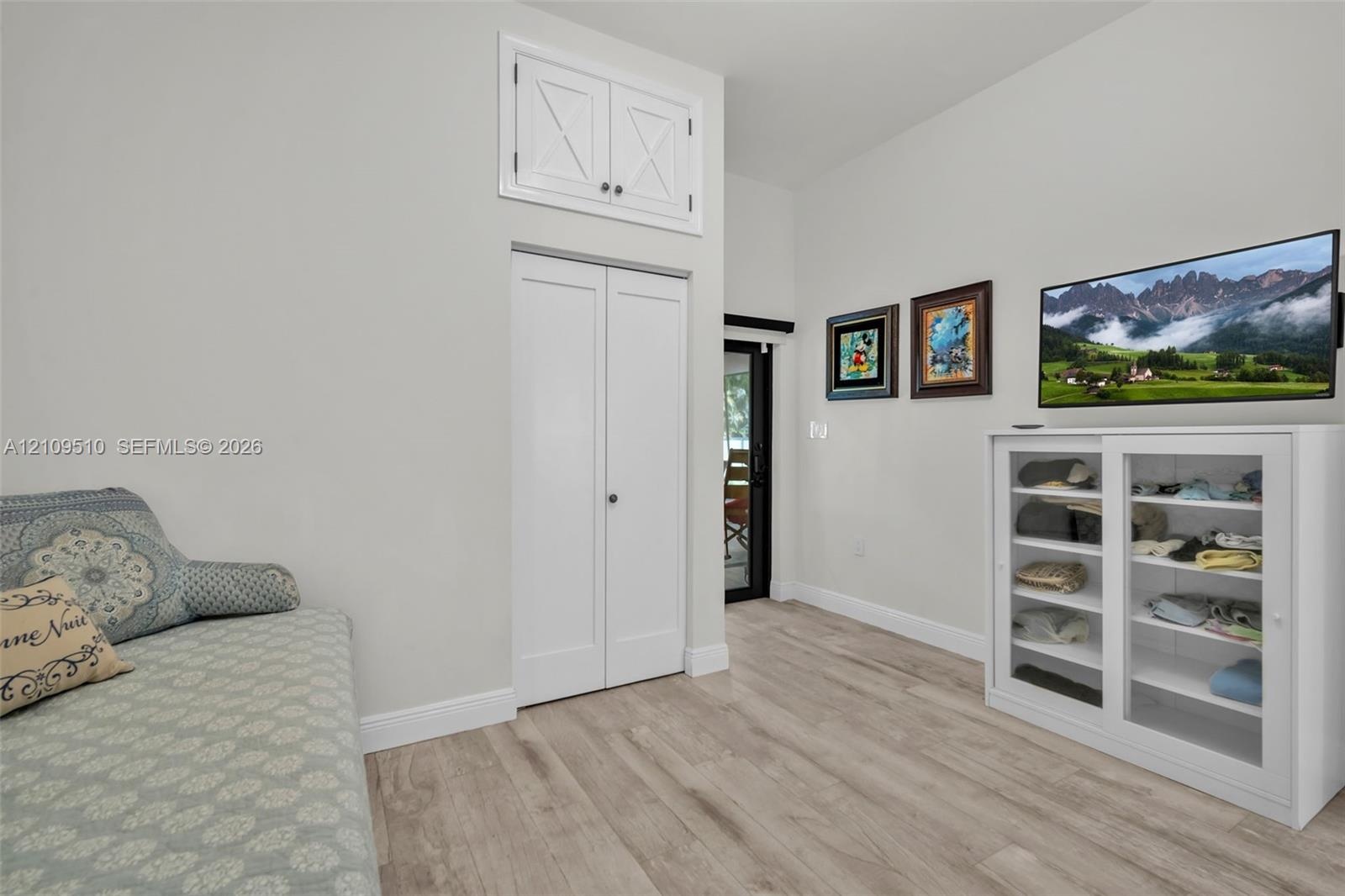Wood-finish flooring, vaulted ceiling, dual-door closet, and upper storage cabinet with X-detail inlay