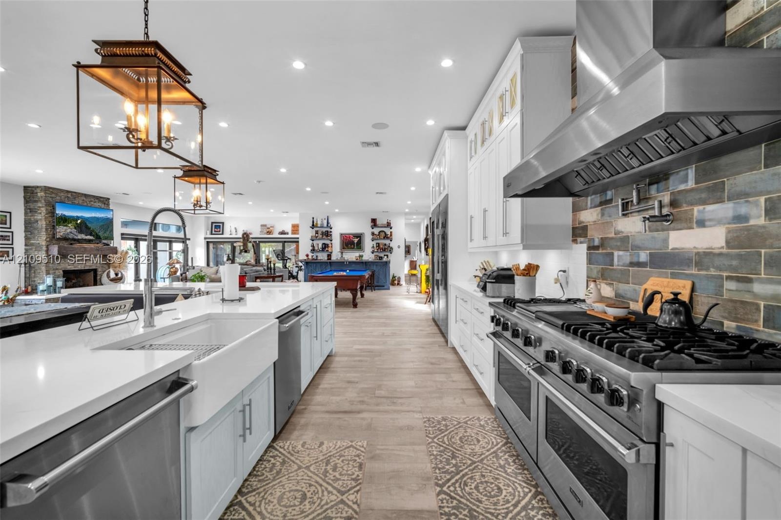 Kitchen featuring white cabinetry, quartz countertops, a farmhouse sink, stainless steel professional-style range with matching hood, and multi-tone s