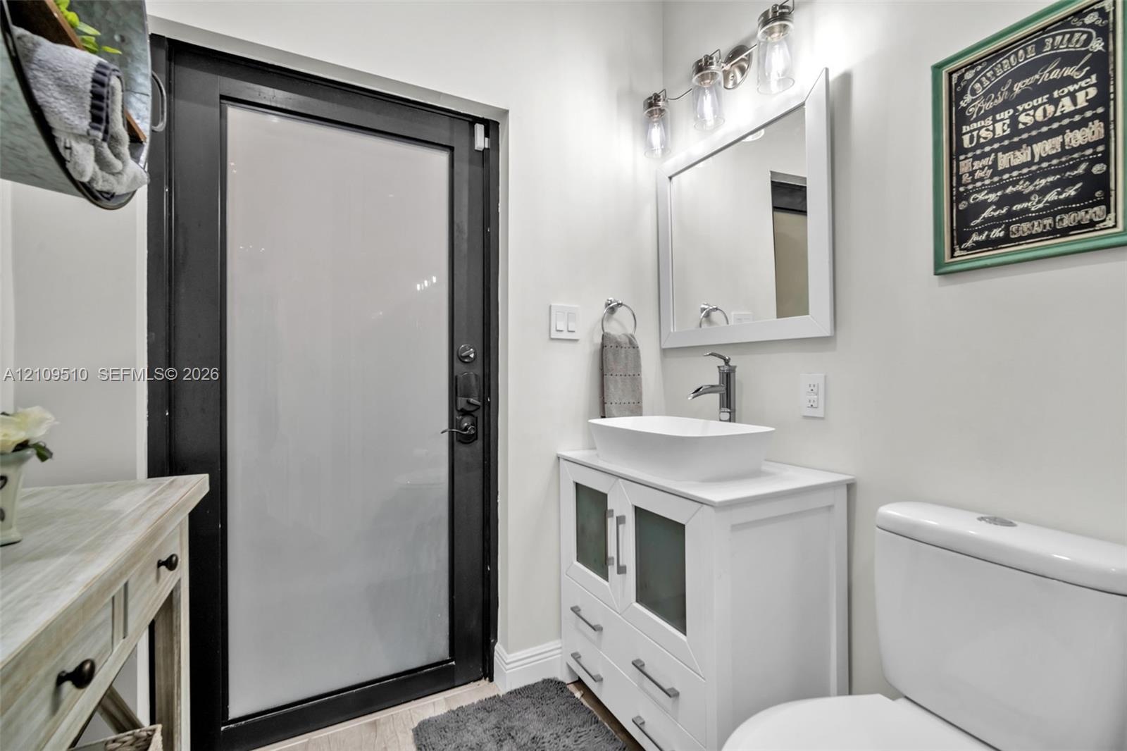 White vanity featuring a rectangular vessel sink, frosted glass cabinet inserts, and brushed nickel hardware, paired with a multi-light fixture, frame