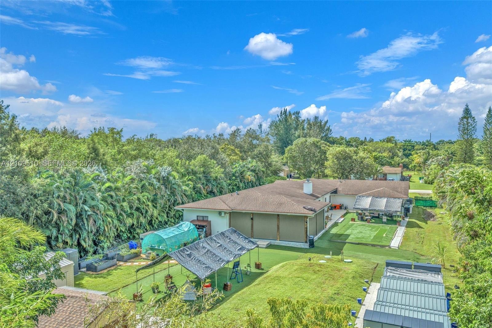 Expansive backyard featuring a sprawling lawn, mature perimeter trees, hardscaped patio, and multiple structural shade coverings