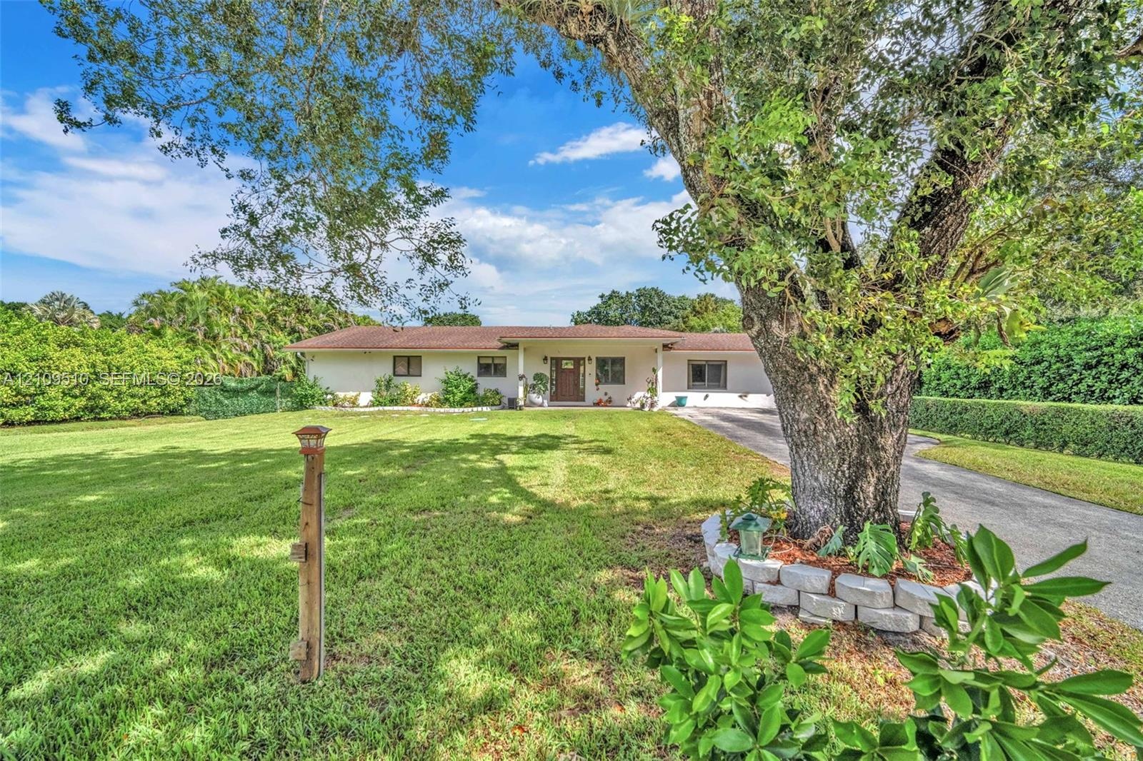 Single-story exterior featuring a light-toned stucco façade, a multi-paneled front entry door, expansive lawn, mature tree, and a concrete paver retai