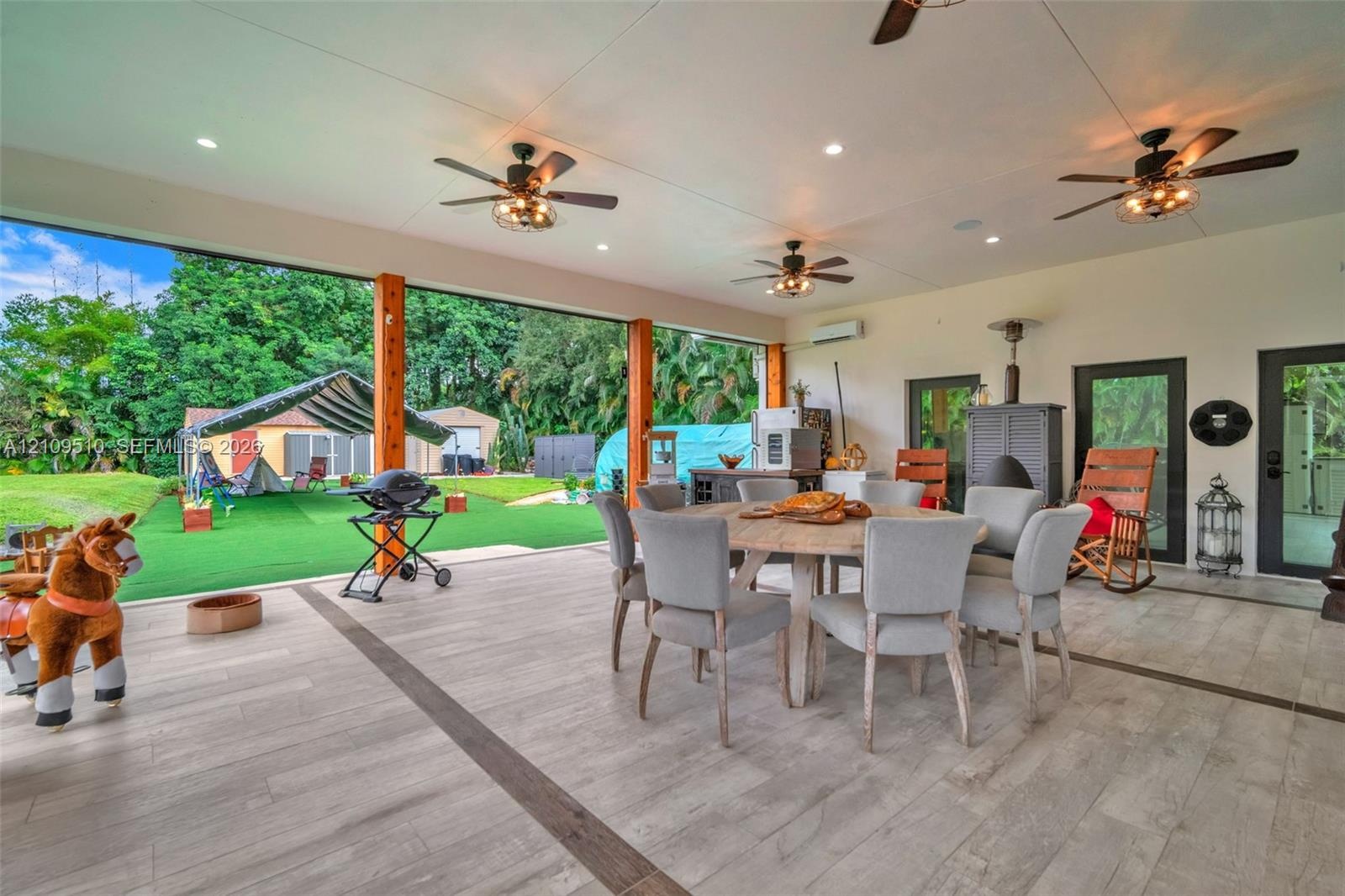 Covered outdoor patio featuring tile flooring with decorative inlay, exposed wood support beams, multiple ceiling fans with integrated lighting, and r