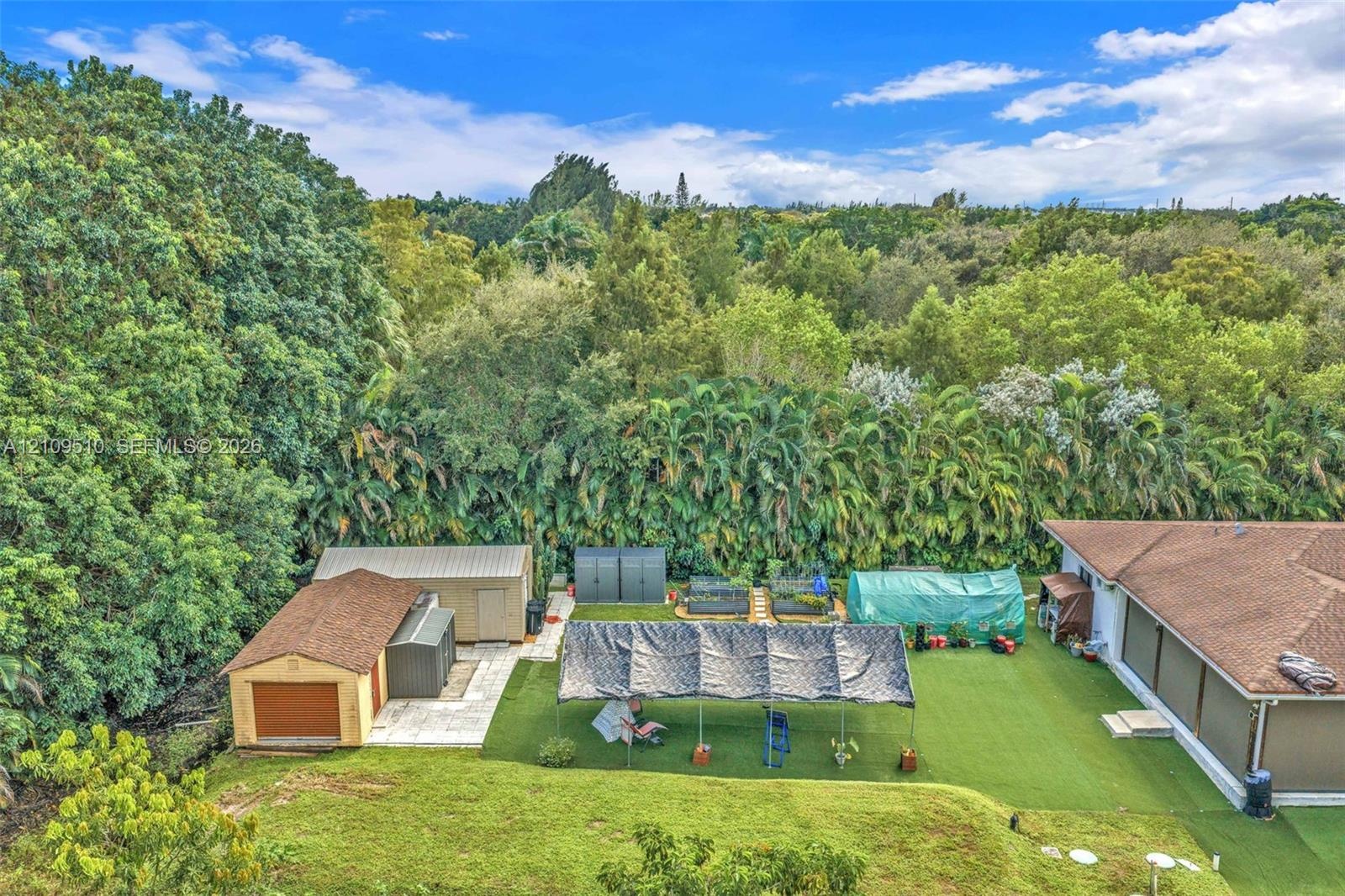 Expansive backyard featuring a synthetic lawn, a detached garage with a shingle roof, paved hardscaping, and mature perimeter trees