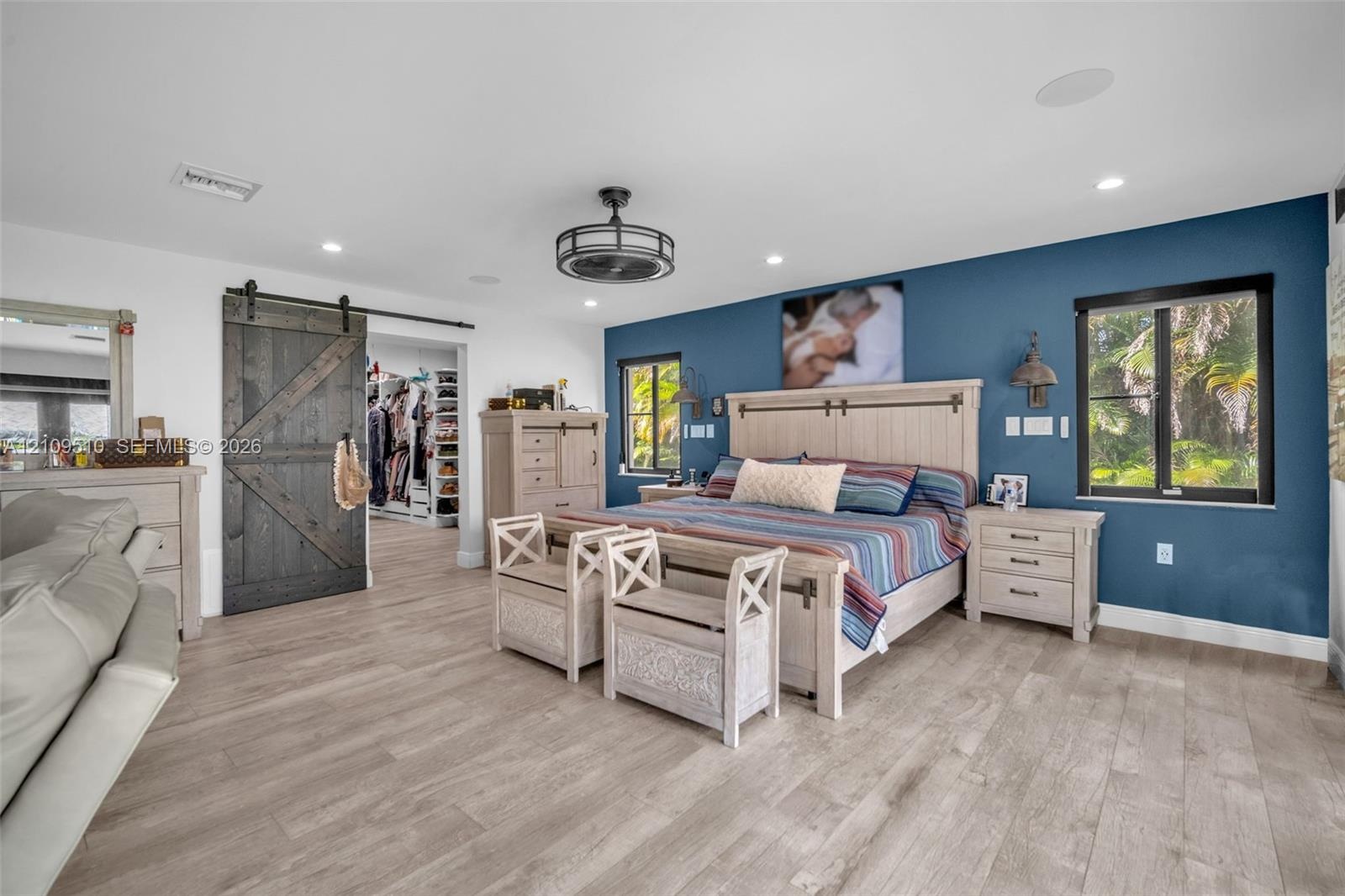 Wood-finish flooring, dark charcoal barn-style sliding door, recessed ceiling lighting, industrial-style drum ceiling fan, and blue accent wall